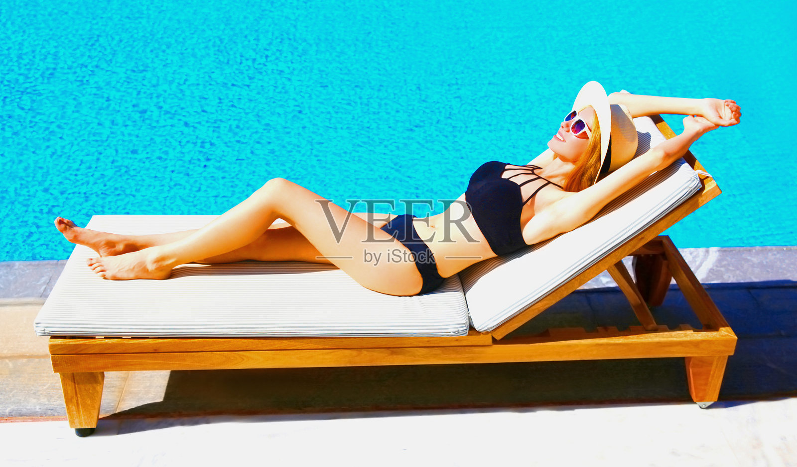 暑假概念-快乐的年轻女子躺在躺椅上放松在蓝色的水池背景照片摄影图片