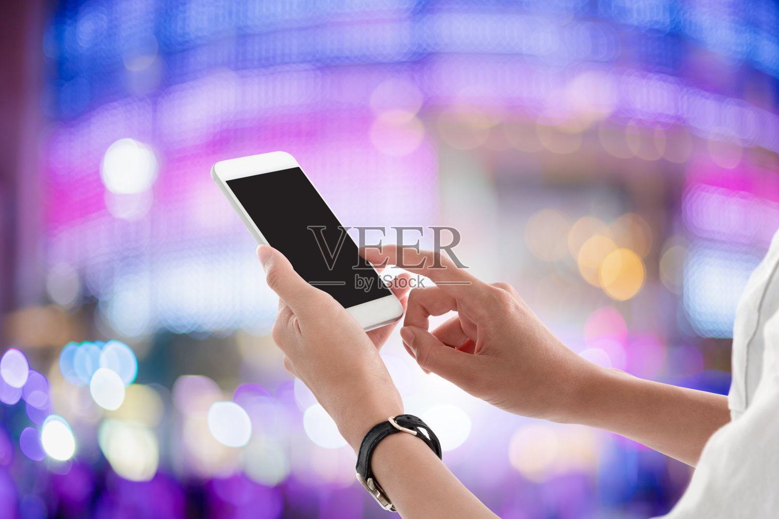 女人手牵着手机，在模糊的商场灯光背景下黑屏发短信或做广告。模拟手机的概念。照片摄影图片
