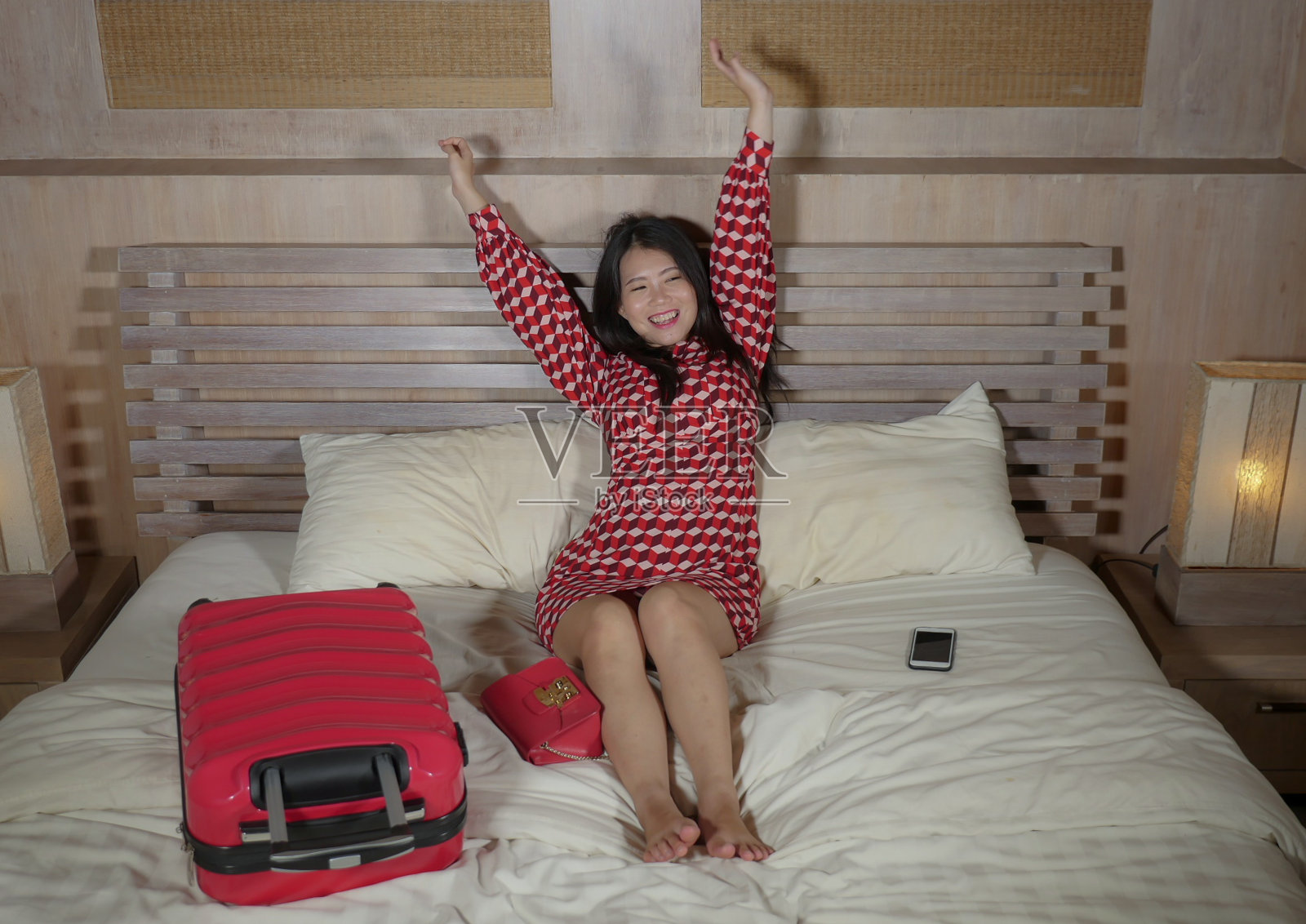 年轻美丽和快乐的亚洲韩国女人穿着时髦的衣服坐在房间的床上，带着行李入住酒店后兴奋和愉快地享受豪华目的地概念假日旅行照片摄影图片