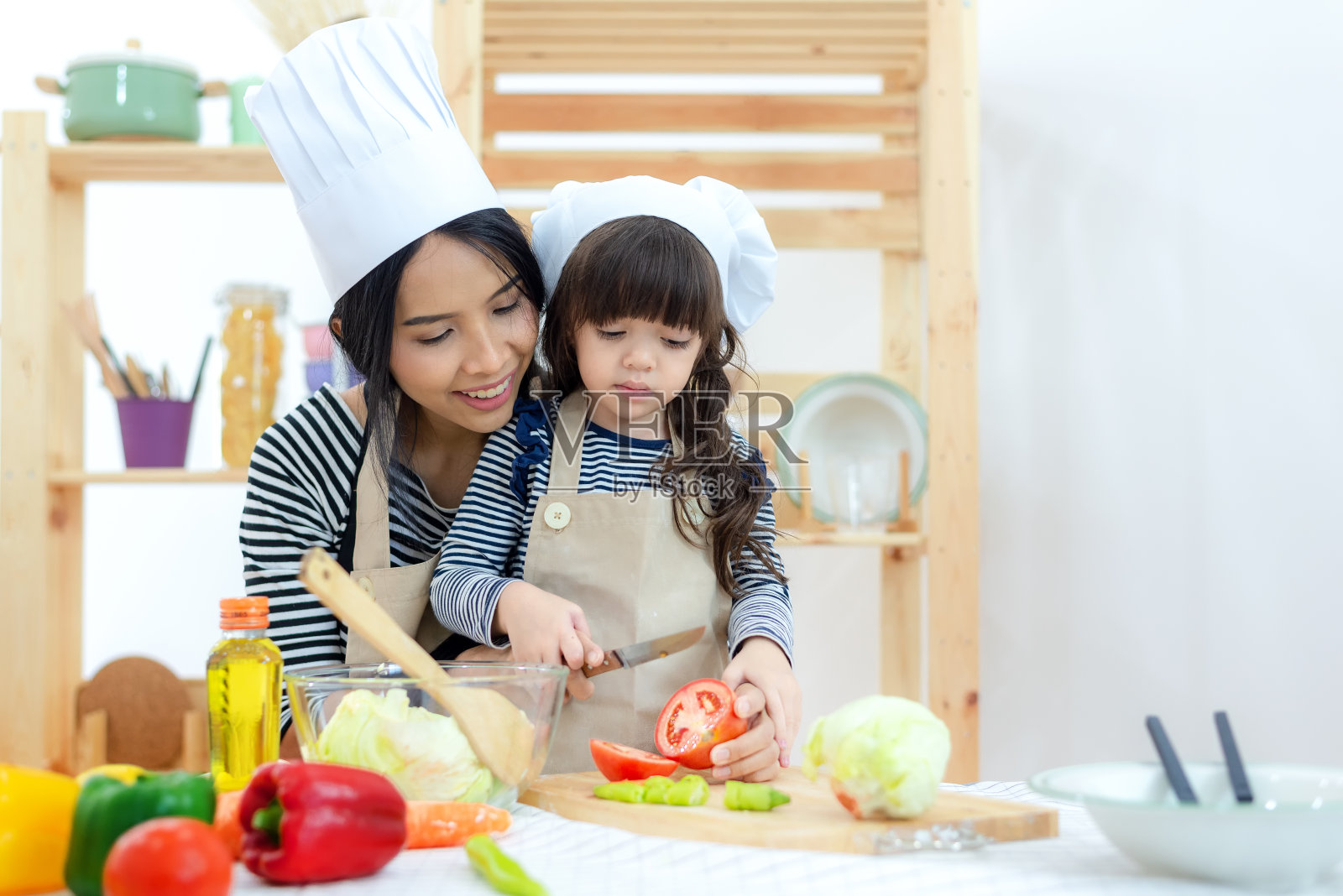 母亲和小女孩在厨房烹饪和切新鲜的蔬菜。家庭生活方式的概念照片摄影图片