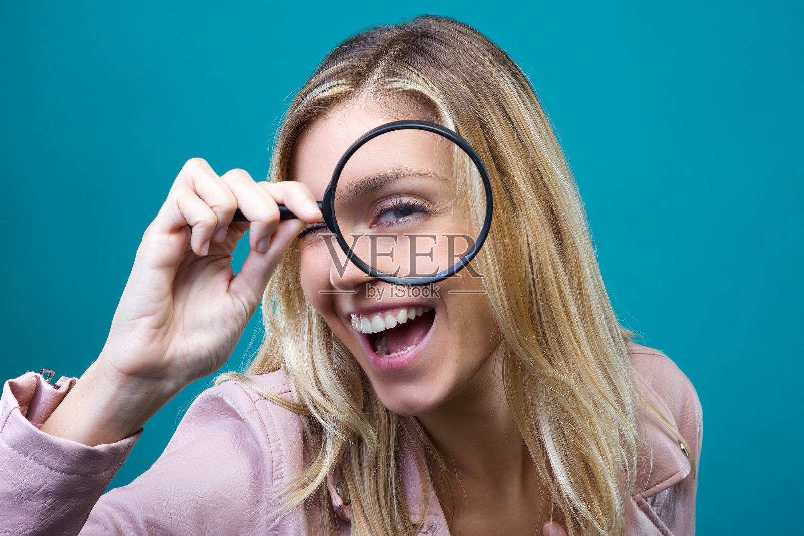 一个快乐的年轻女人透过放大镜看着蓝色的背景。照片摄影图片
