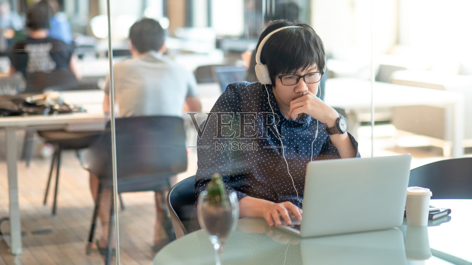 年轻的亚洲商人戴着眼镜和耳机与笔记本电脑在共同的工作空间。男性数字游牧民利用数字平台从事自由职业。物联网概念。照片摄影图片