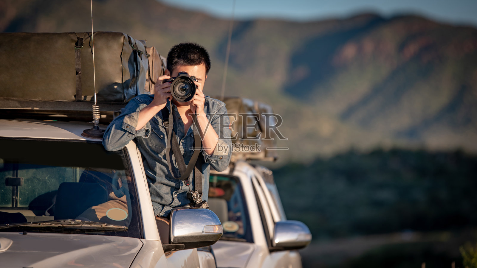 年轻的亚洲男子旅行者兼摄影师坐在车窗上拍摄非洲纳米比亚公路旅行的照片。旅行摄影的概念照片摄影图片