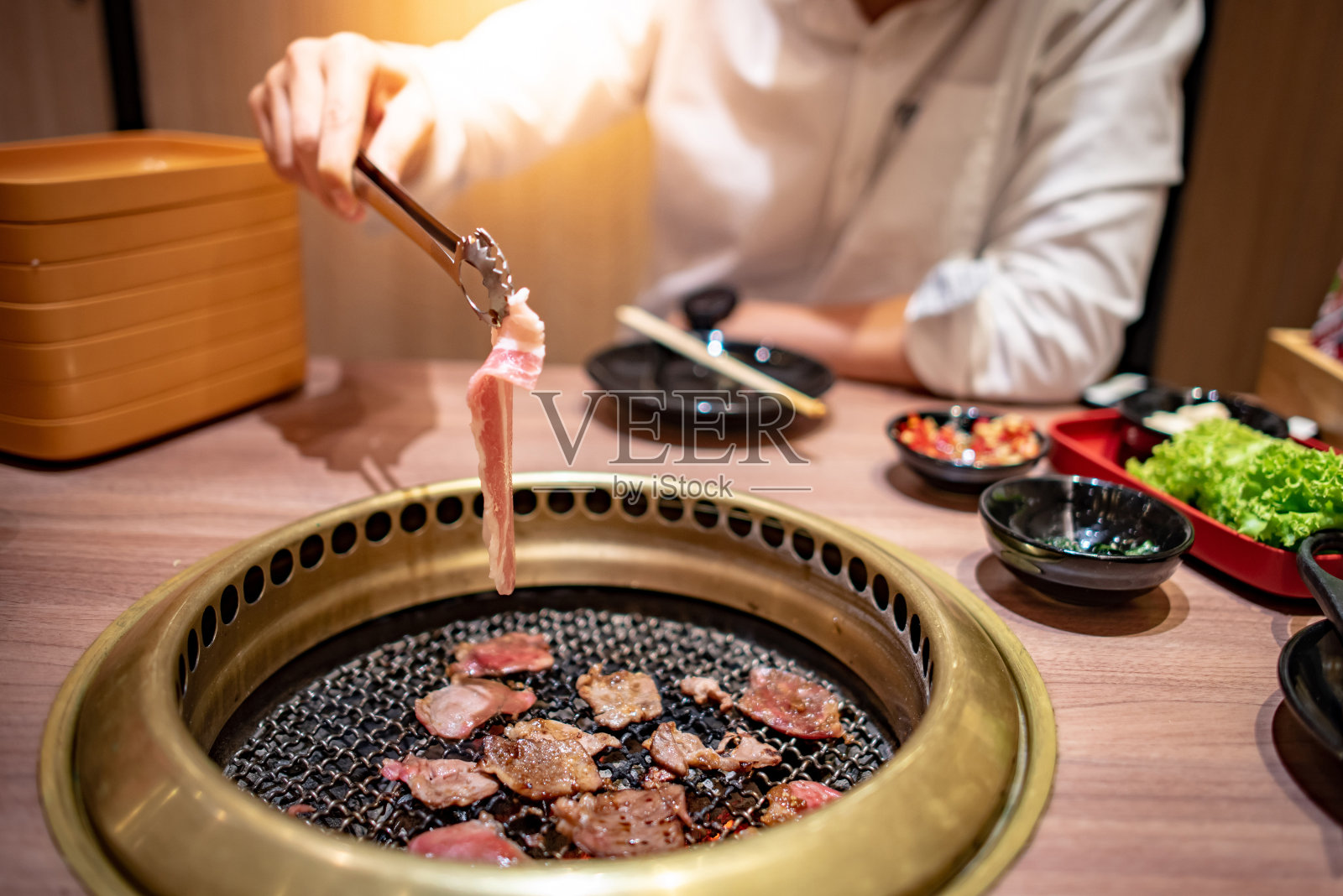 亚洲男子用夹钳在烤盘上烤牛肉和培根。在餐厅享用韩国烧烤自助餐。照片摄影图片