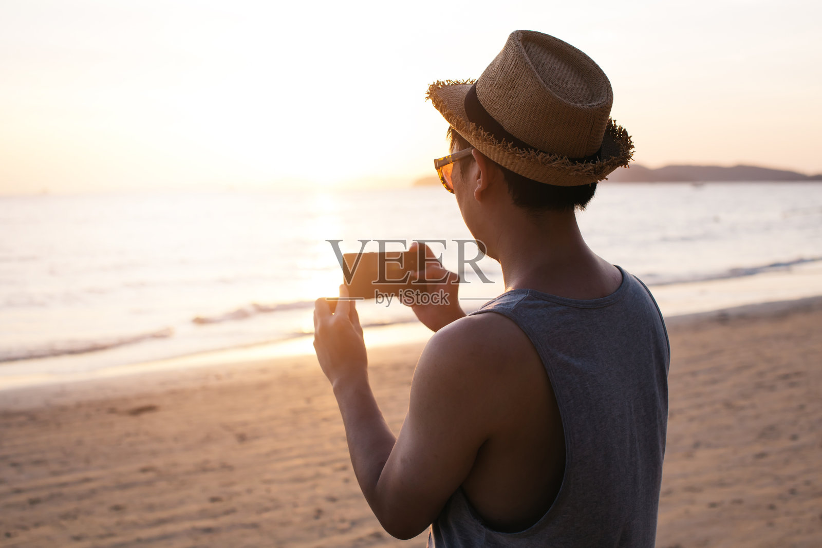 剪影的背影年轻男性旅行背包客与帽子拍照的夏天海滩风景日落-旅游照片瞬间捕捉概念照片摄影图片