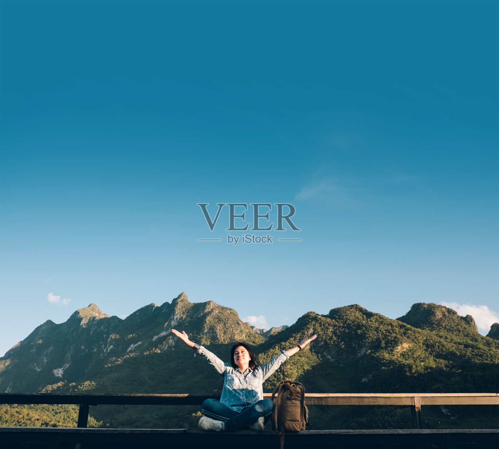 亚洲妇女旅行者坐在和手臂在空中的观点平台在风景的山与云和蓝天在阳光灿烂的一天在森林。背包客探索自然生活。照片摄影图片