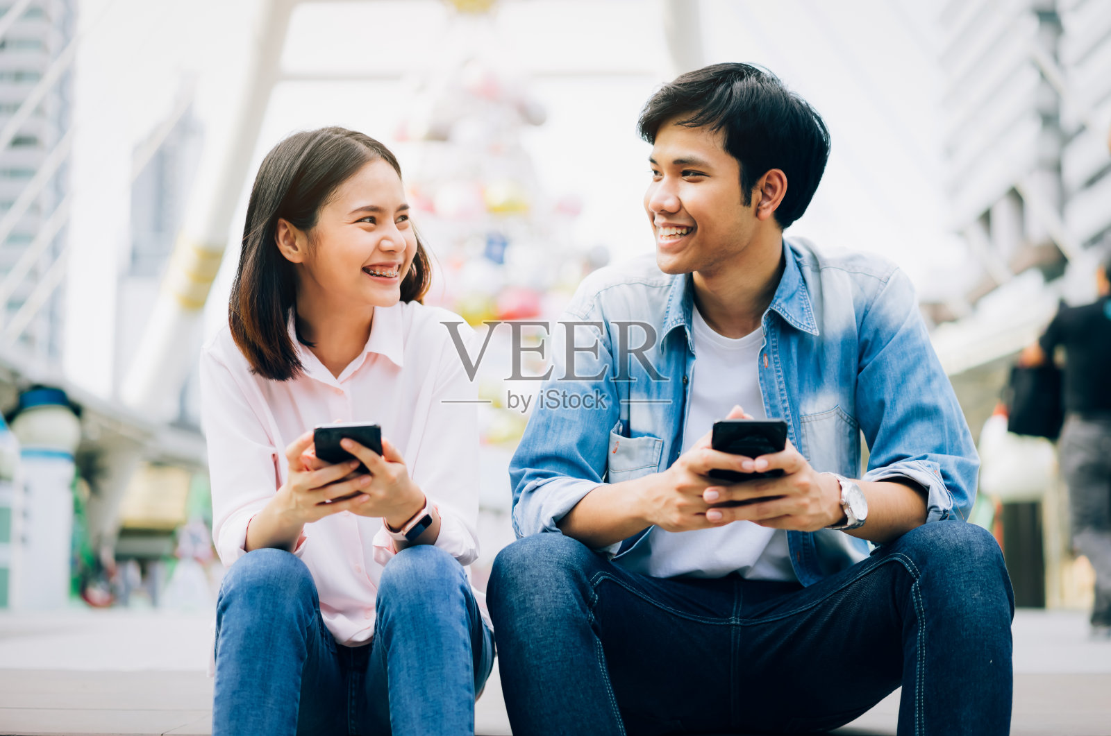 年轻人正在使用智能手机，坐在空闲时间微笑。技术概念照片摄影图片