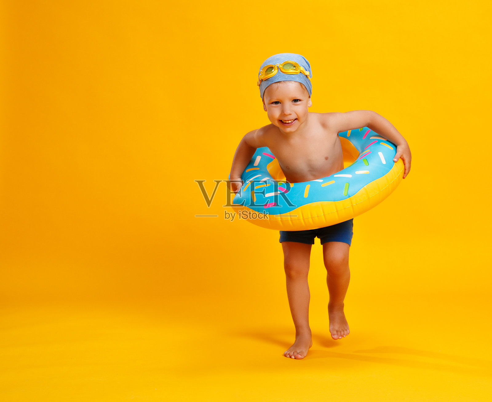 快乐的孩子男孩在泳衣与游泳圈甜甜圈在彩色黄色的背景照片摄影图片