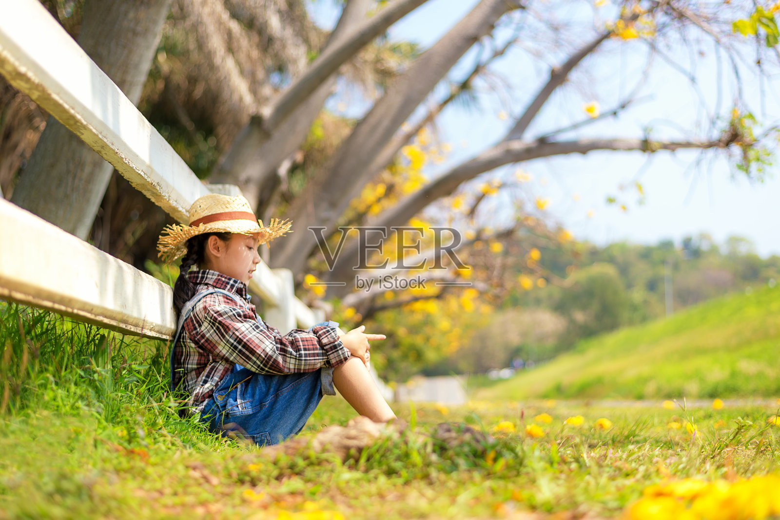 亚洲小女孩坐在户外的落叶在秋天的公园，快乐和放松在夏季和假期。生活方式的概念照片摄影图片