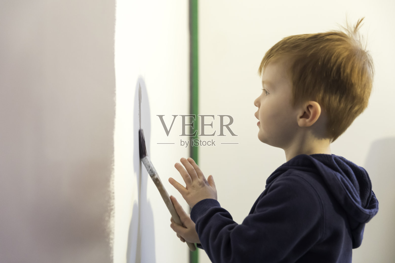小男孩学习如何油漆他的房子的墙壁照片摄影图片