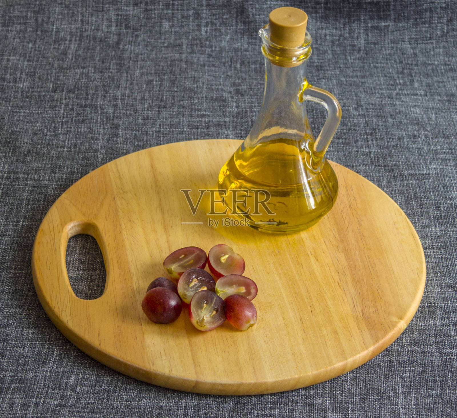 一个小玻璃罐里放着油和碎葡萄。在一块木头砧板上照片摄影图片