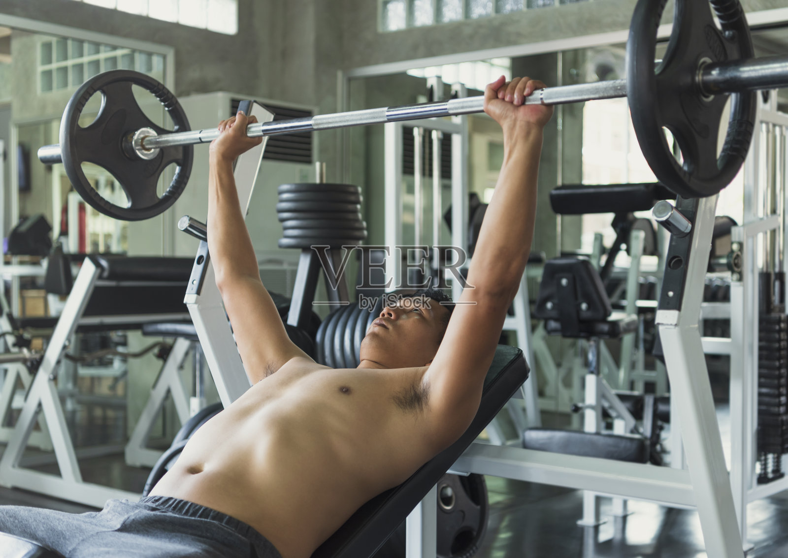 年轻的亚洲男子在健身房举杠铃。健康的生活方式和锻炼动机的概念。照片摄影图片