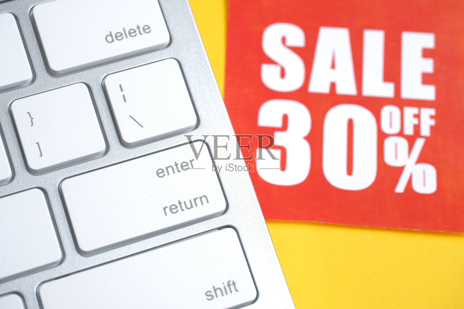 白色键盘上黄色背景的红色纸标签上写着“降价30%”。照片摄影图片