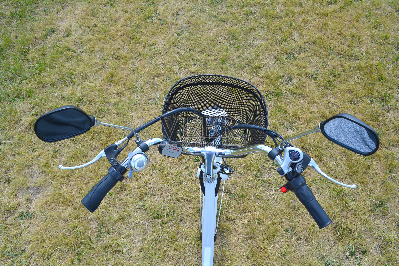 电动自行车的舵或舵在阳光明媚的夏日公园里。从上面。电动自行车的方向盘带有车铃、刹车、速度开关、动力电池控制装置和后视镜。照片摄影图片