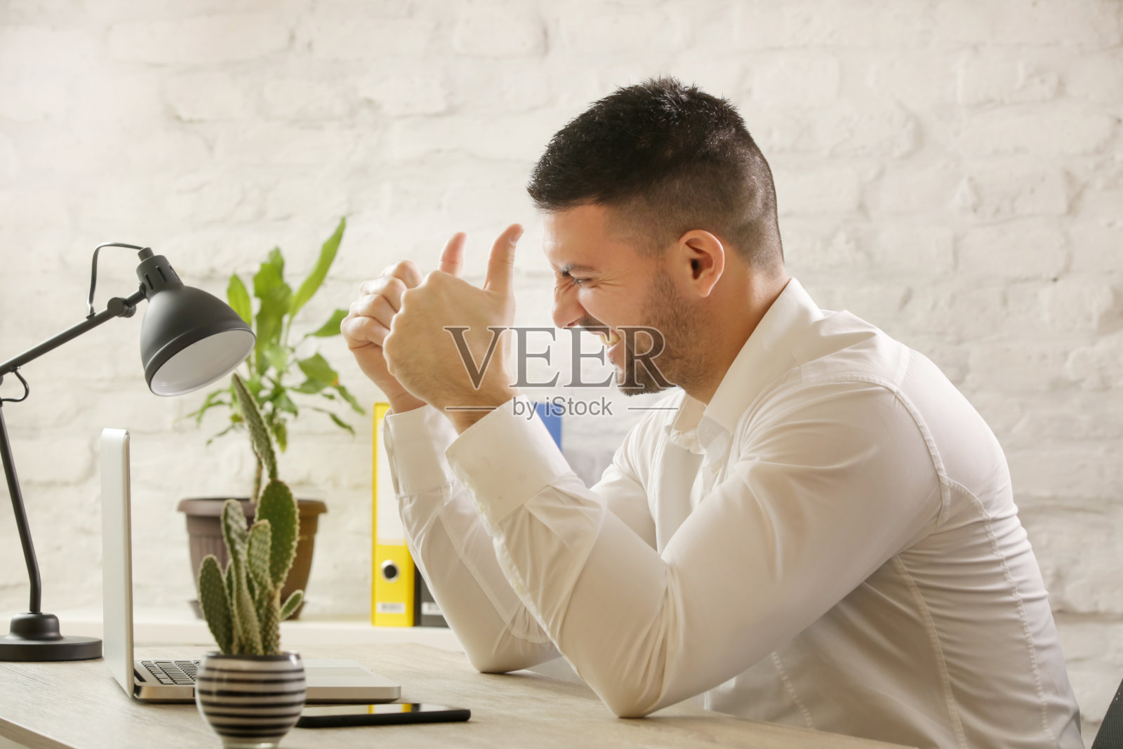 这是一个年轻愉快的商人坐在他的办公桌前，看着笔记本电脑，竖起大拇指。办公室里成功的一天。照片摄影图片