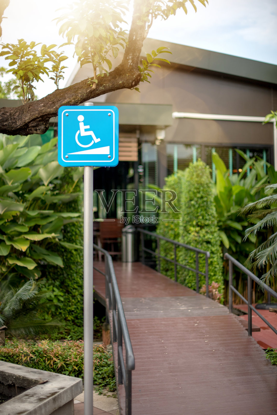障碍坡道进入标志。通往大楼的轮椅通道，由一个白色的蓝色方形覆盖着残疾人在轮椅上的形象和坡道组成。照片摄影图片
