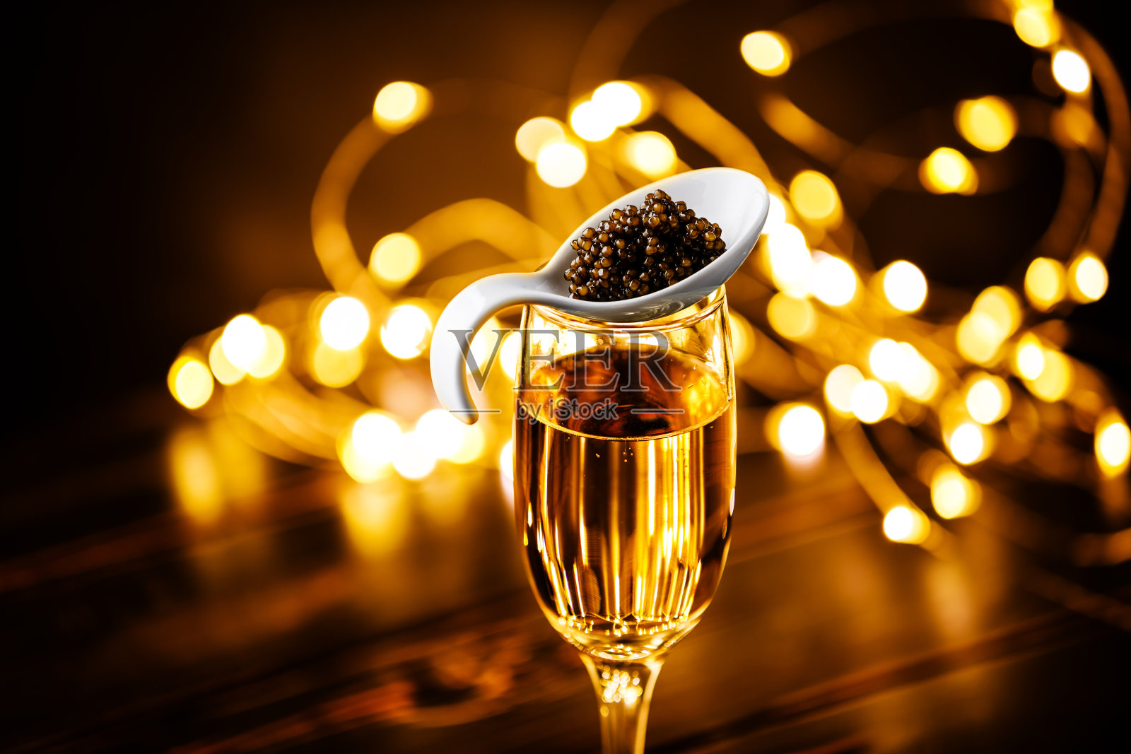 黑鱼子酱在瓷勺和香槟杯自助餐桌上风格的节日圣诞闪闪发光的灯光背景bokeh照片摄影图片