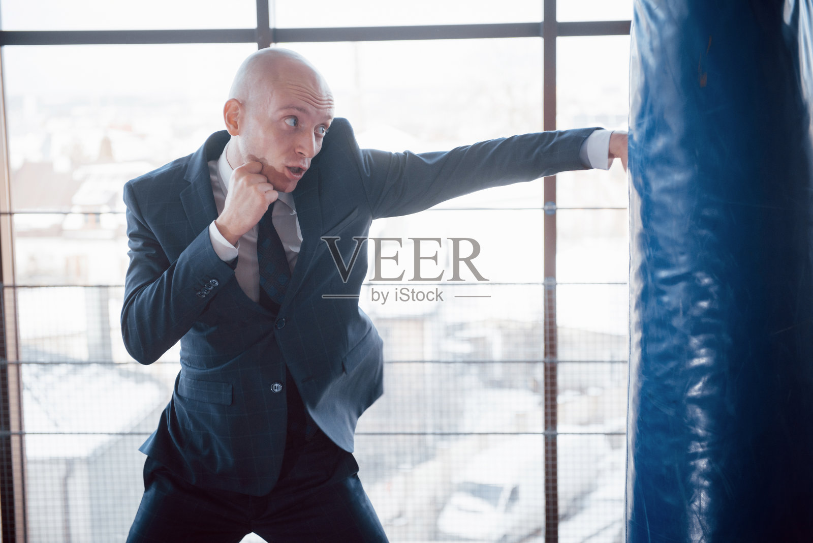 一个愤怒的秃顶商人在健身房打拳击梨。愤怒管理概念照片摄影图片