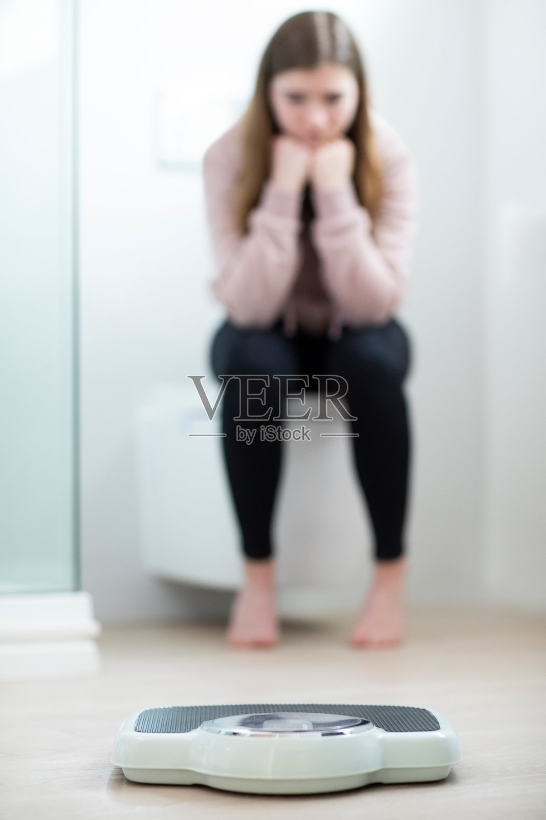 不快乐的少女坐在浴室里看秤照片摄影图片