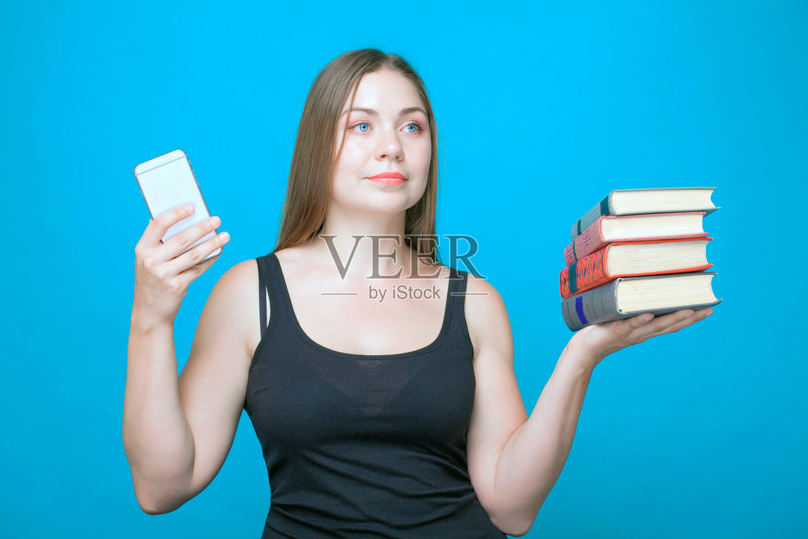 年轻漂亮的白人女人左手拿着书，右手拿着手机。照片摄影图片
