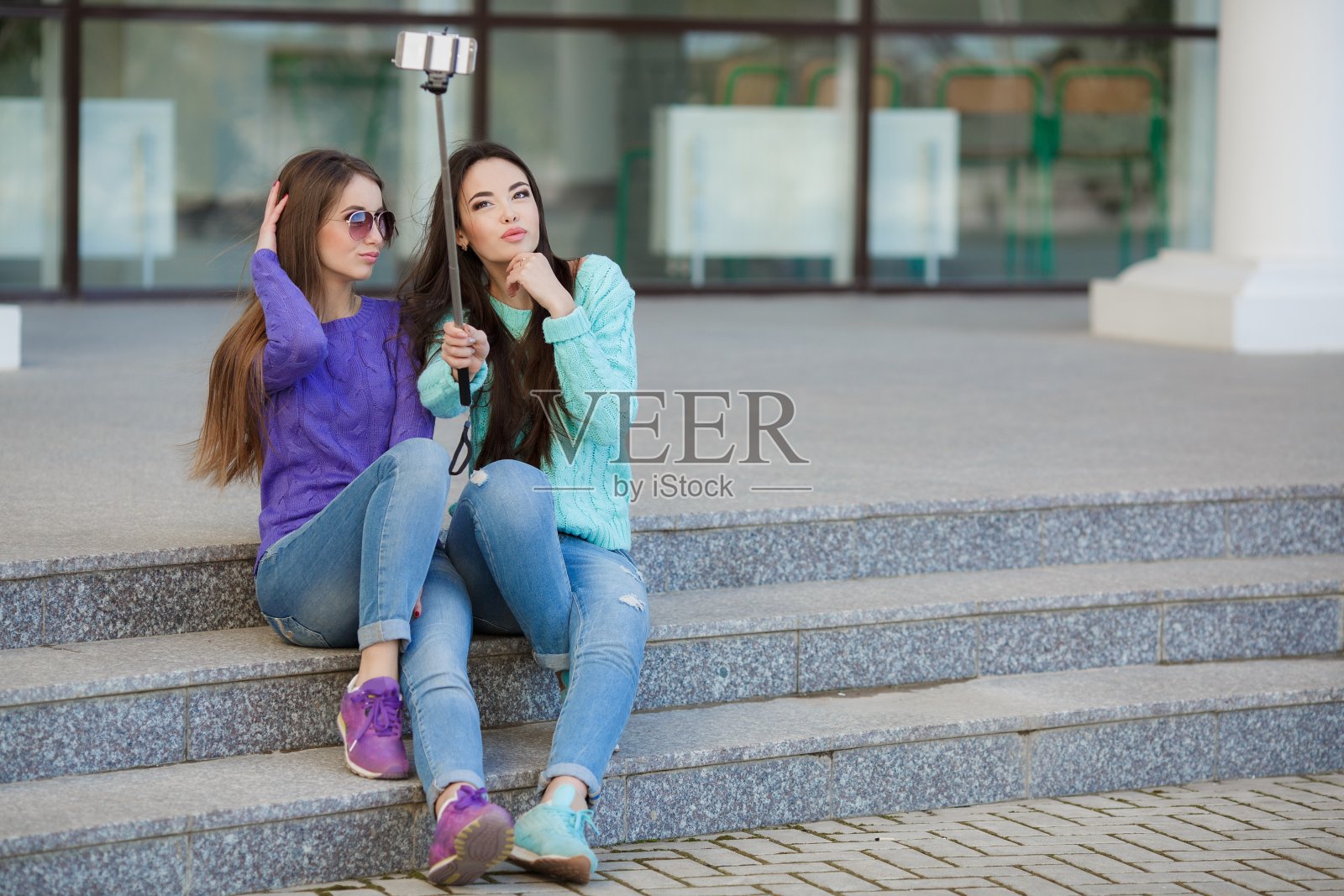 两名年轻迷人的女子在大街上用智能手机拍照。照片摄影图片