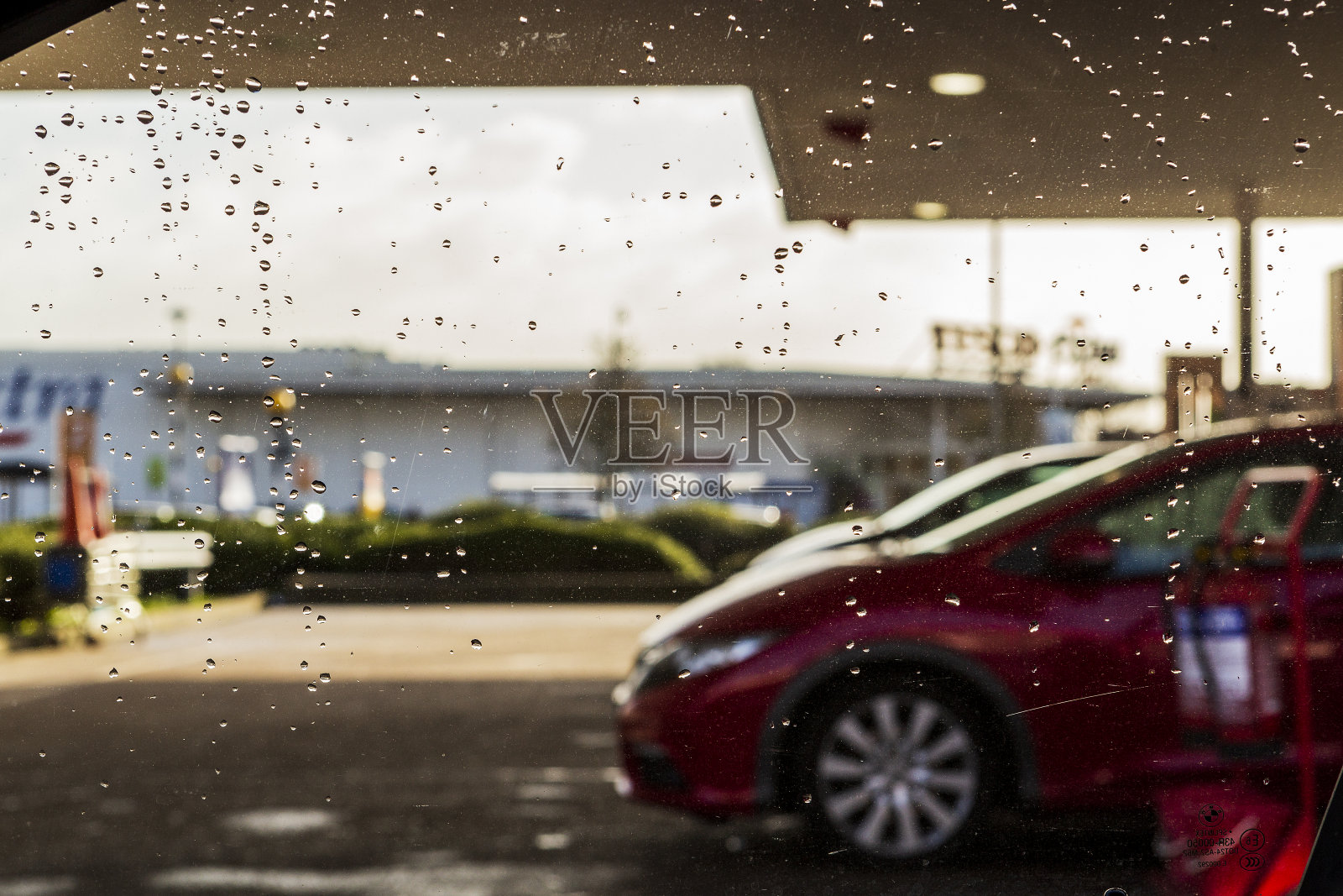 加油站的车窗上滴落着雨滴，背景模糊不清的是一辆车。照片摄影图片