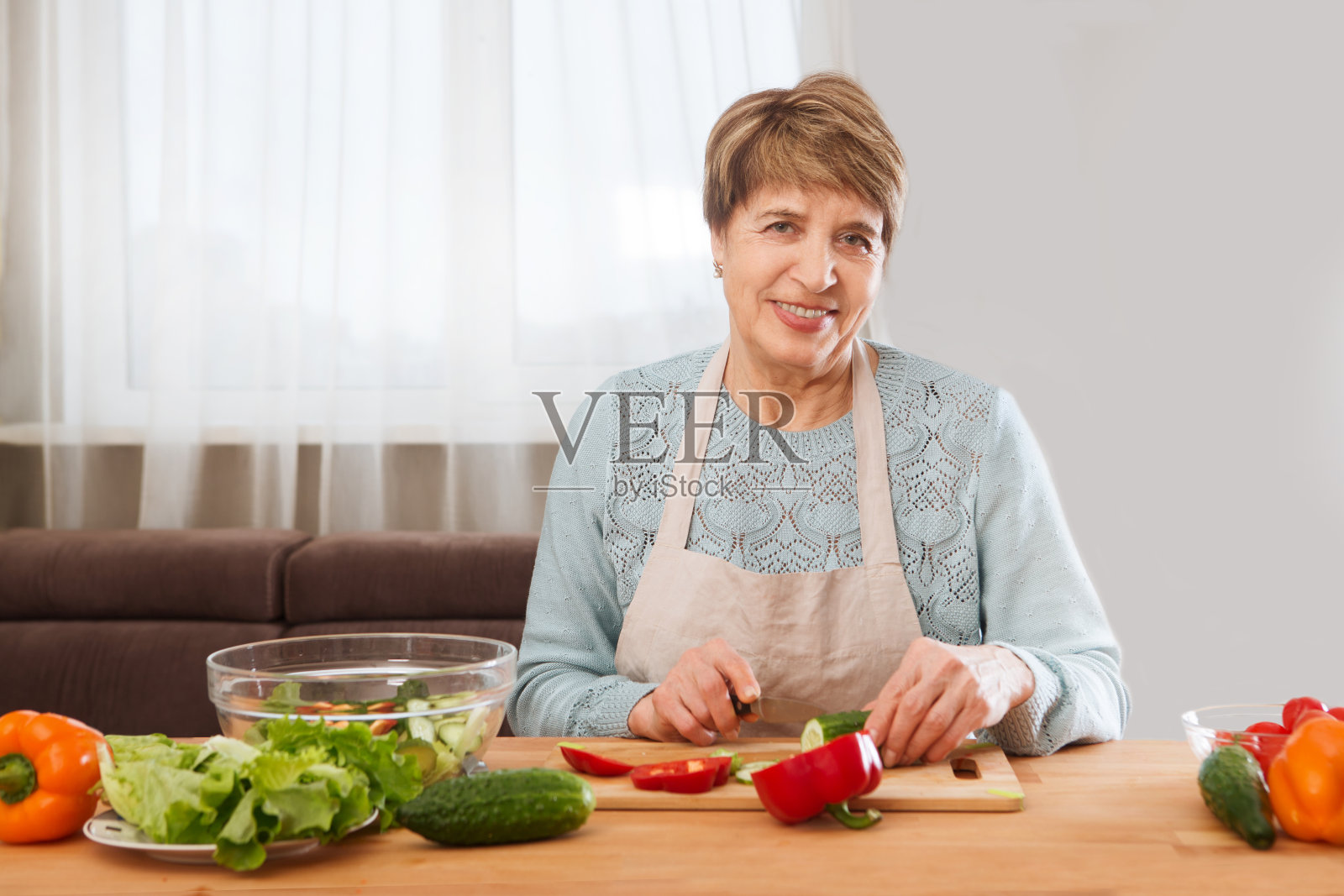 年长的妇女在厨房里做沙拉，看着镜头。健康食品的概念。健康的生活方式。照片摄影图片