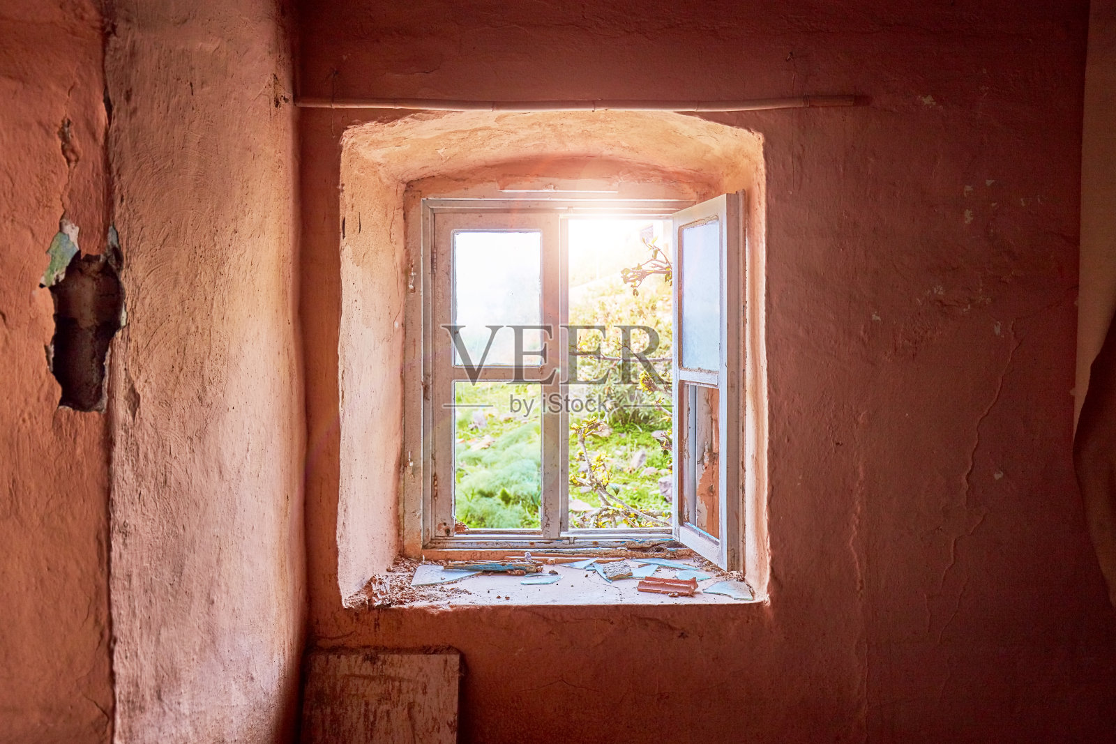 一个废弃的旧农舍的内部，浅粉色的墙壁和一个破损的木窗框，可以看到乡村绿色的草地景观照片摄影图片