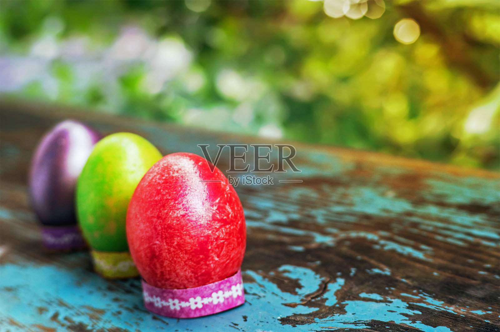 木桌上放着三个五颜六色的复活节彩蛋。照片摄影图片