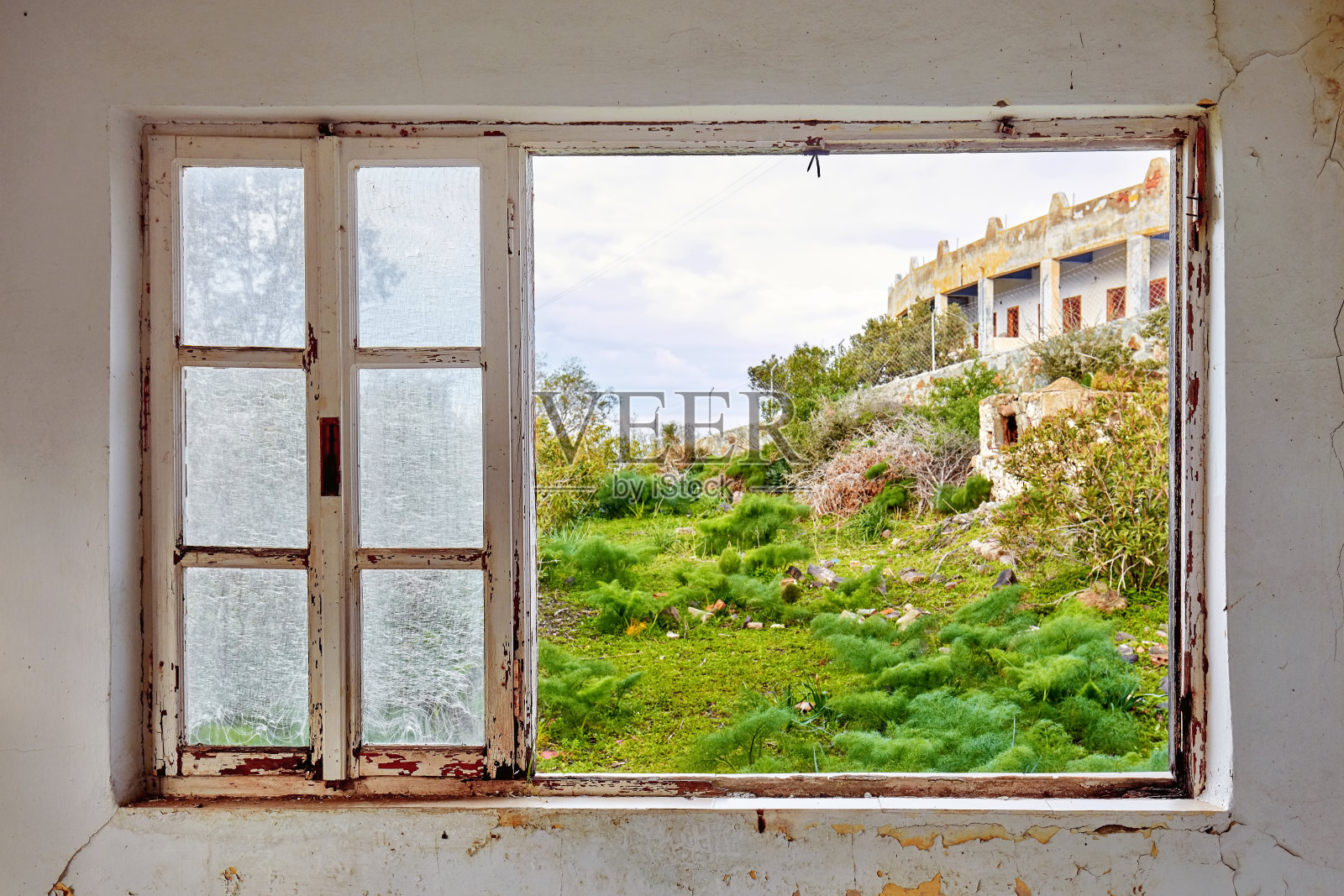 一个破旧的房子的内部，一个破碎的窗框，观看绿色的草地田野景观照片摄影图片