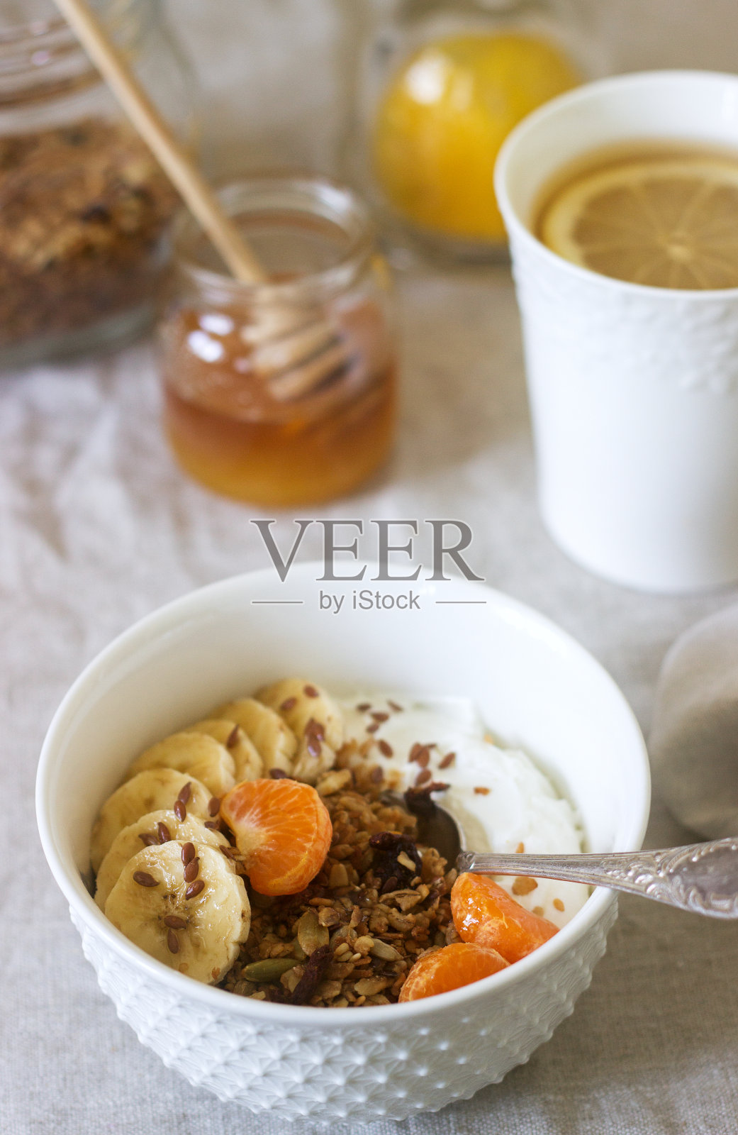 早餐是格兰诺拉麦片、酸奶、茶和亚麻桌布上的连翘花。乡村风格。照片摄影图片