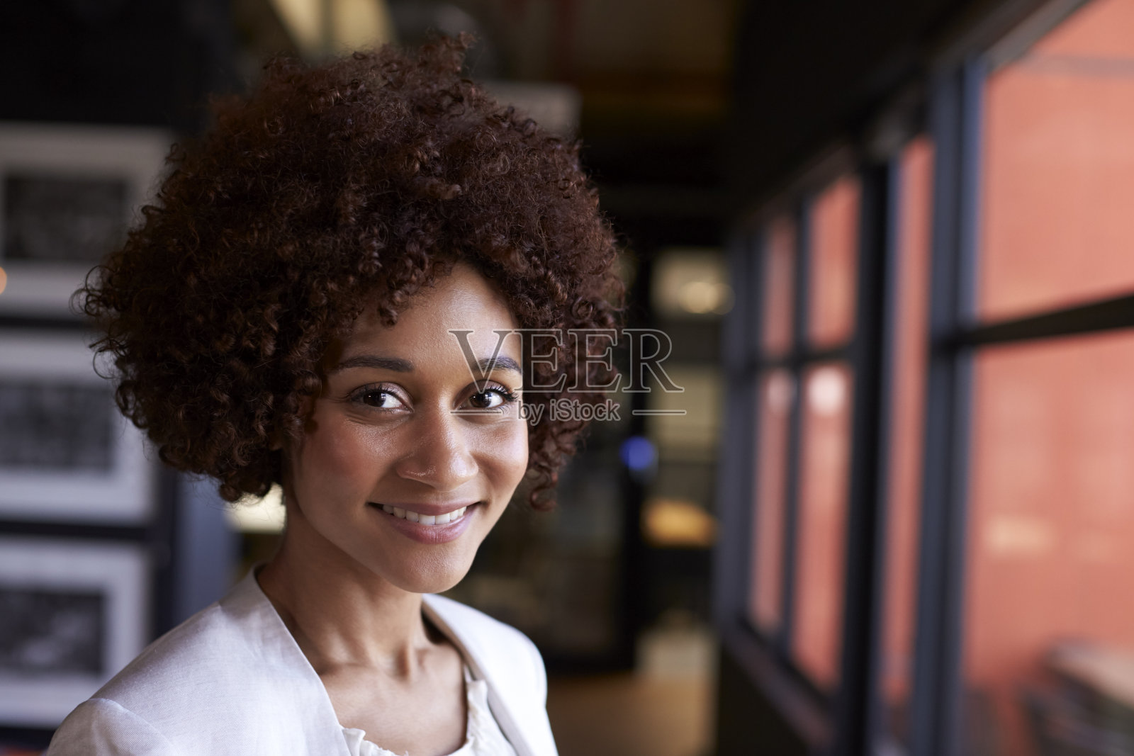 千禧一代黑人女商人在一间办公室的窗口对着镜头微笑，特写照片摄影图片