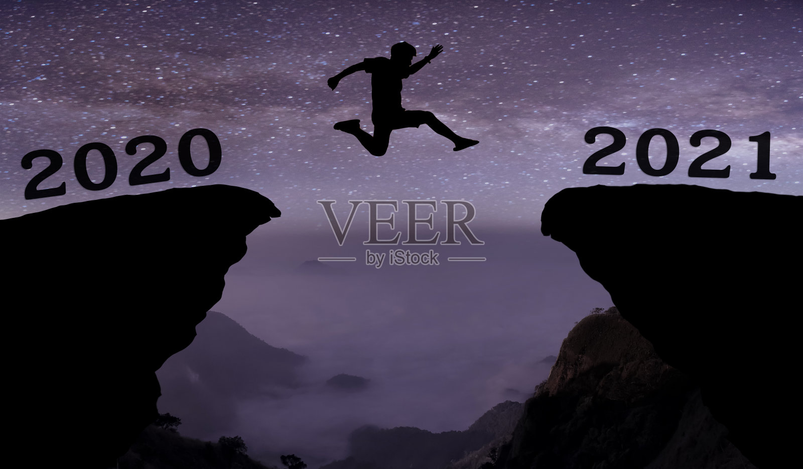 一名年轻男子飞跃2020年至2021年之间的夜空与星星，穿过山沟上剪影的黄昏多彩的天空。2021年新年快乐。照片摄影图片