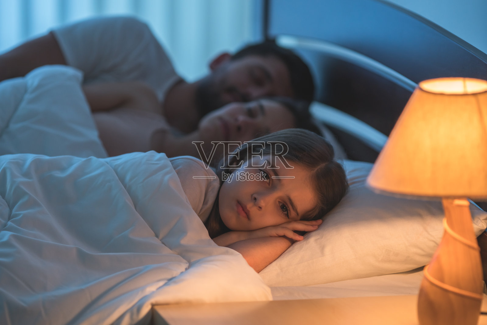 女孩躺在睡觉的父母旁边。晚上的时间照片摄影图片