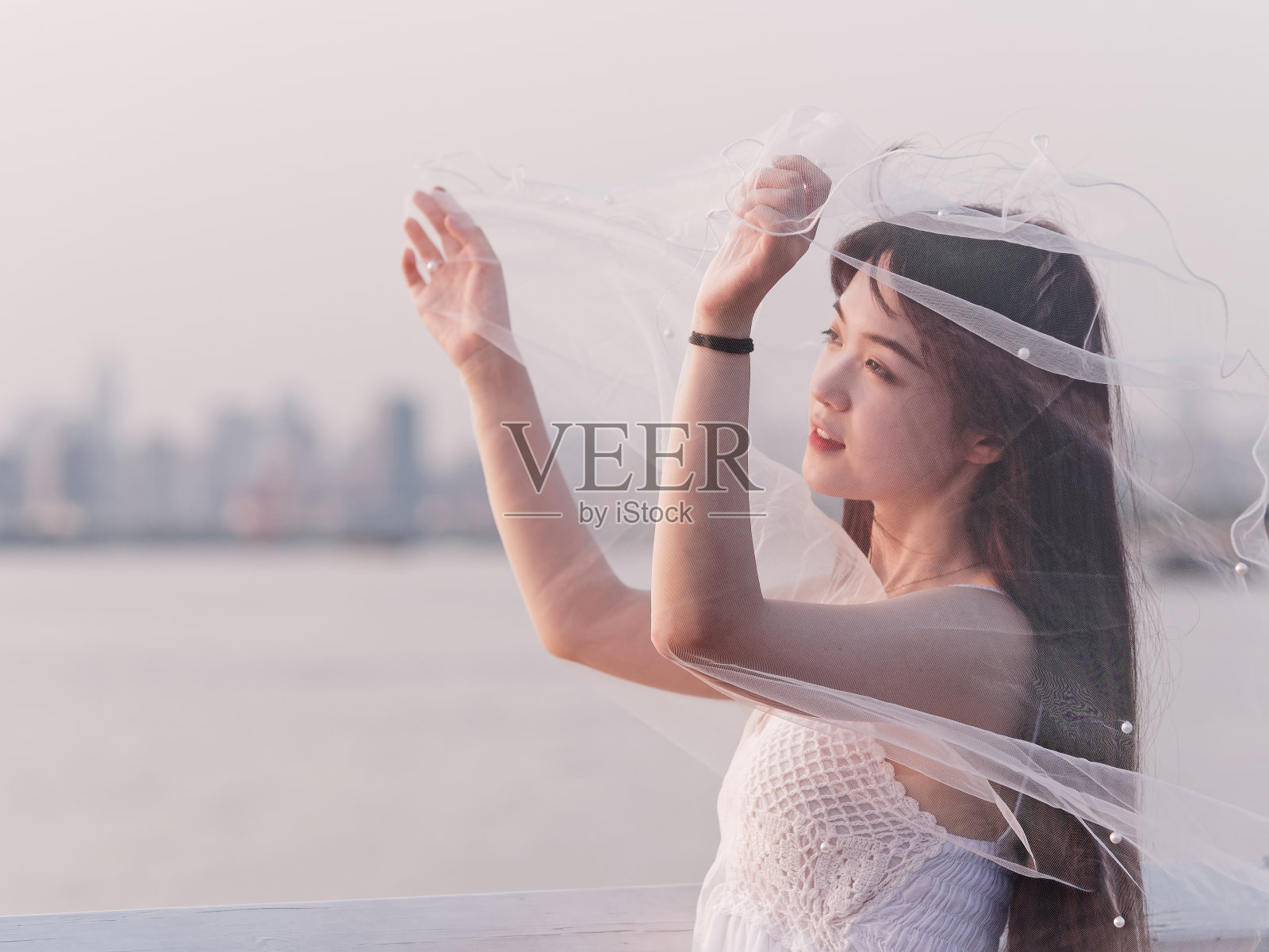 美丽的中国女孩的肖像在白色新娘礼服看在风黄昏与模糊的河流水背景，美丽，生活方式和夏天的概念。照片摄影图片