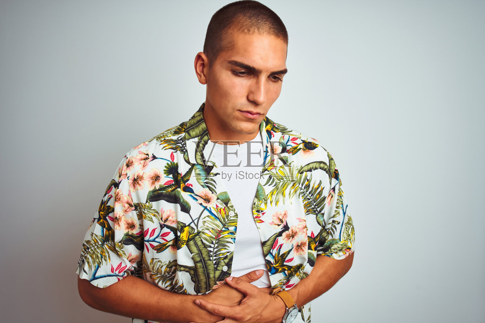 年轻英俊的男子在假期穿着夏威夷衬衫在白色的背景与手胃，因为消化不良，痛苦的疾病感觉不舒服。疼痛的概念。照片摄影图片