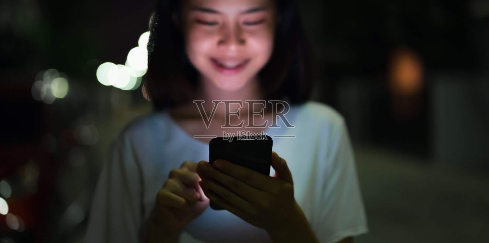 一个女人拿着智能手机在晚上的街道上的特写。通讯技术的概念。照片摄影图片