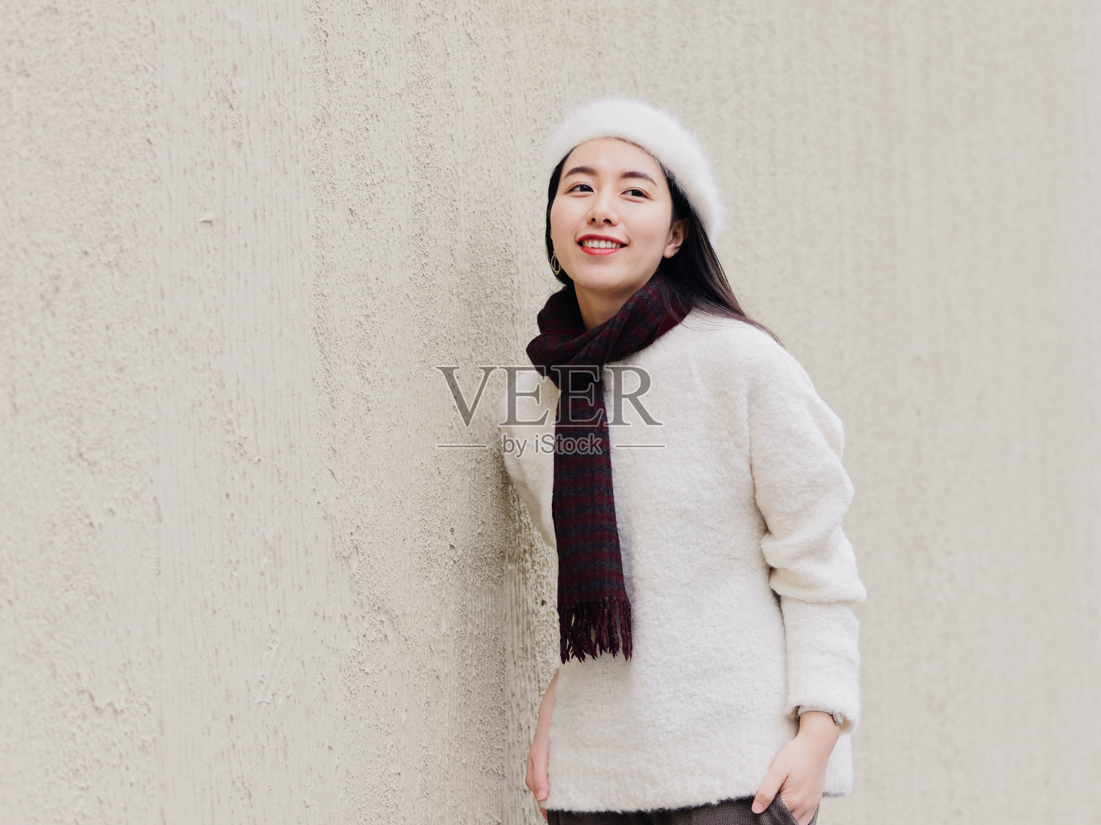 美丽年轻的黑发女人在白色贝雷帽和羊毛衫微笑与街道墙的背景。户外时尚写真魅力中国年轻开朗时尚淑女，街头摄影。照片摄影图片