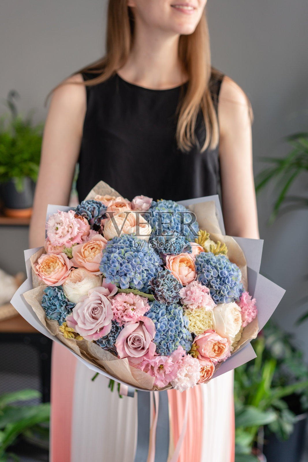 女人手里拿着一束美丽的混合鲜花。花店概念。英俊的新鲜的花束。花交付。蓝色和粉色照片摄影图片