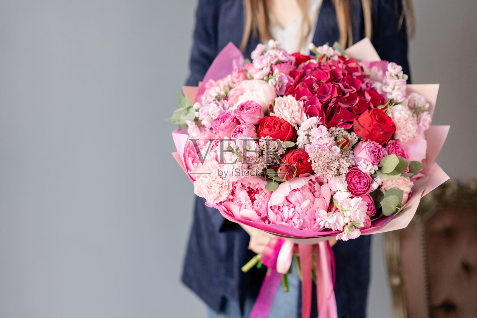 粉色的牡丹和红色的绣球花。女人手里拿着一束美丽的混合鲜花。花店概念。英俊的新鲜的花束。花交付。红色和粉红色。照片摄影图片