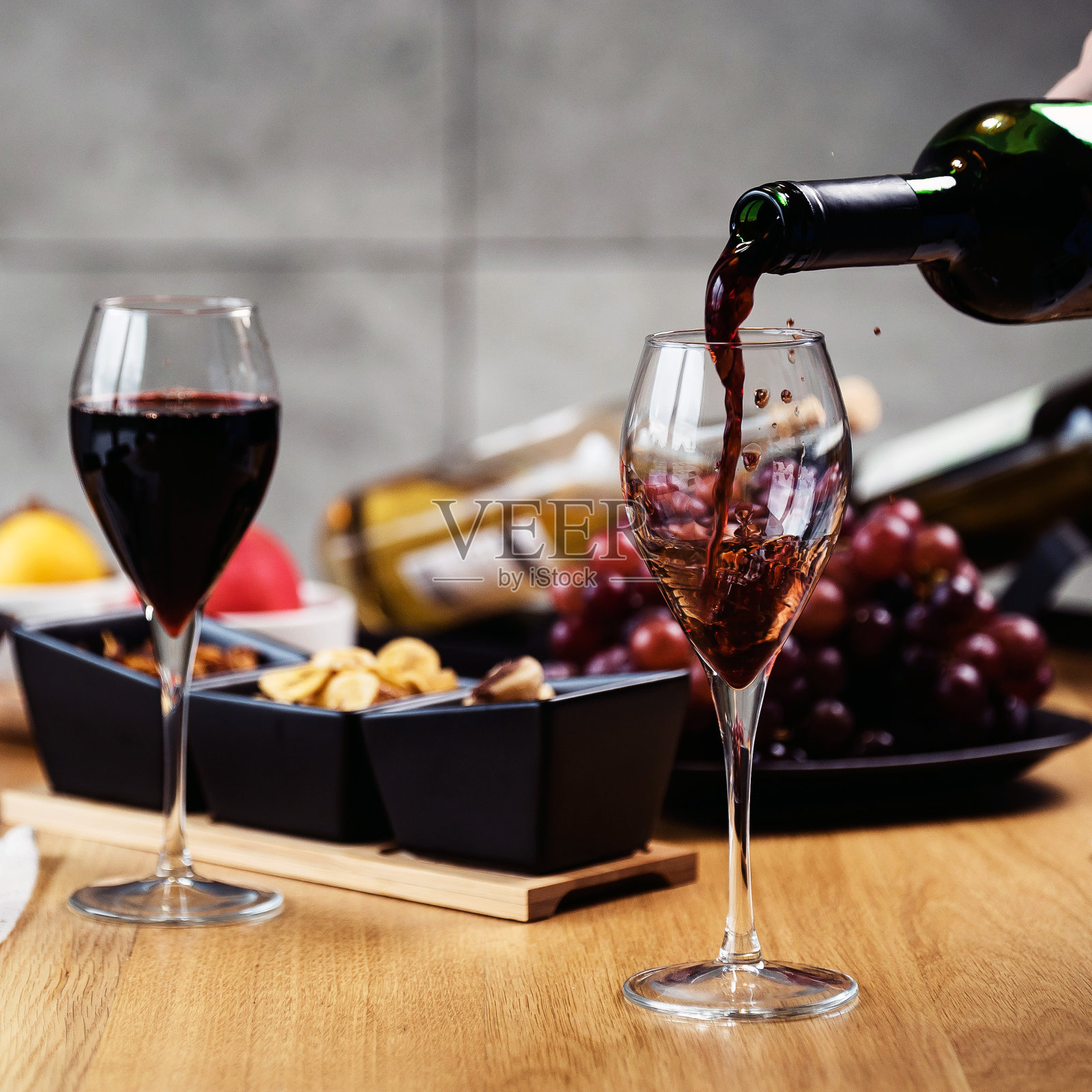 在品尝各种各样的开胃菜时，将红酒倒入酒杯中。照片摄影图片