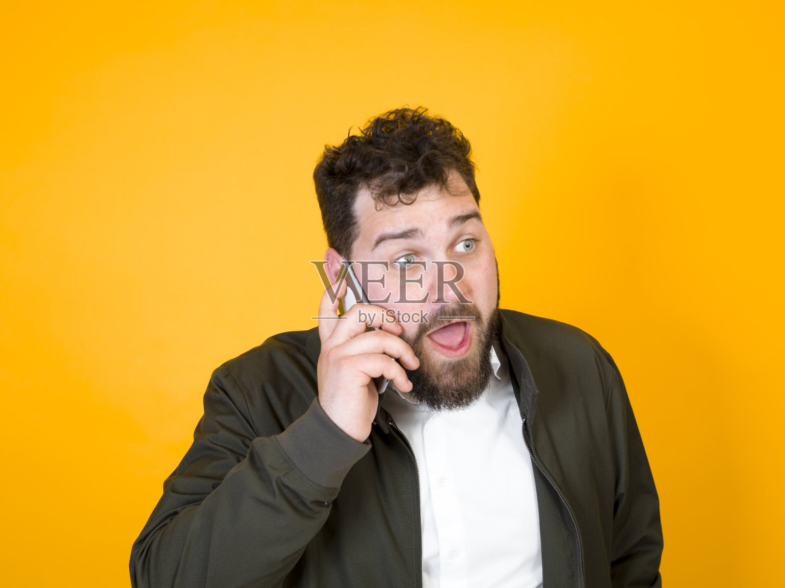 黑胡子黑头发的酷男人拿着智能手机在橙色背景前摆造型照片摄影图片