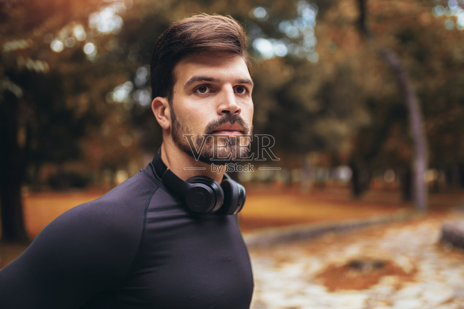 一个年轻男子的肖像在一个早晨慢跑在秋天的公园，男子听着音乐与耳机照片摄影图片