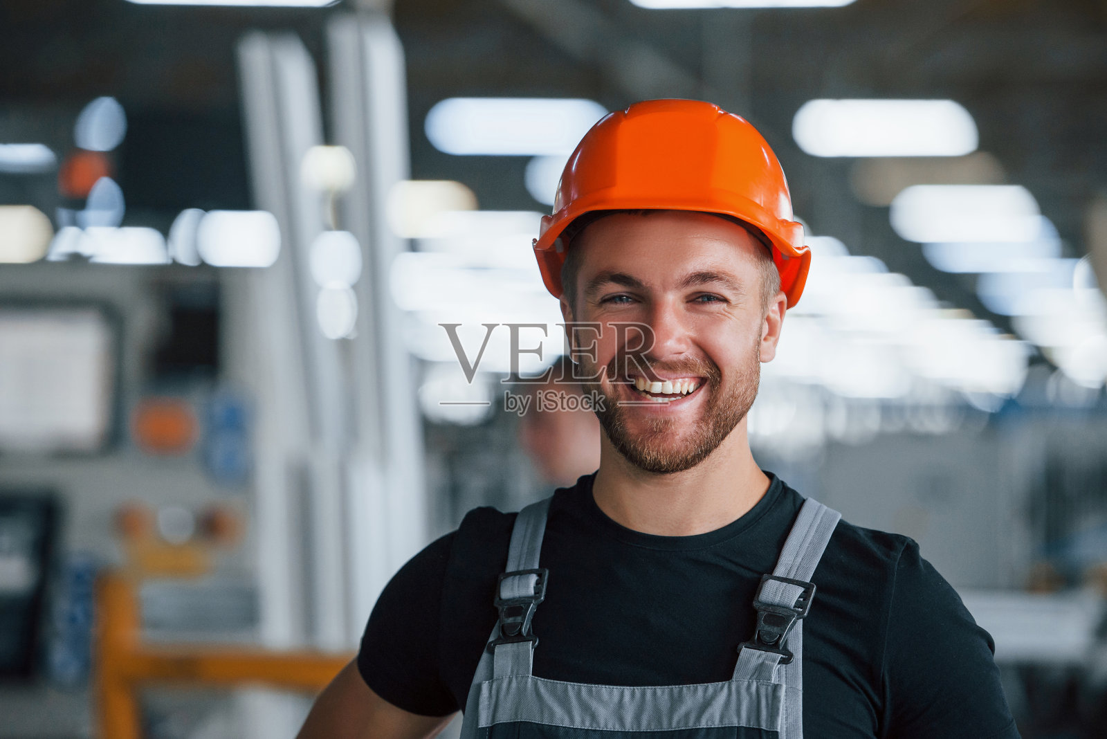 微笑和快乐的员工。工业工人在工厂室内的肖像。戴着橙色安全帽的年轻技术员照片摄影图片