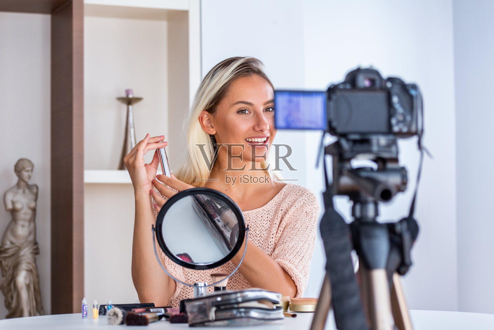 年轻的女士谈论化妆品拿着化妆调色板而录制她的视频。一个女人在为她的化妆品博客制作视频。照片摄影图片