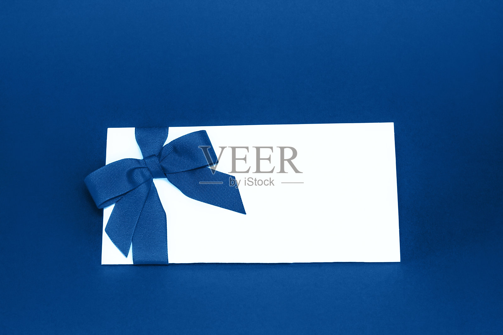 孤立的白色礼品卡与时尚的蓝色丝带蝴蝶结在蓝色背景。节日贺卡的概念。照片摄影图片