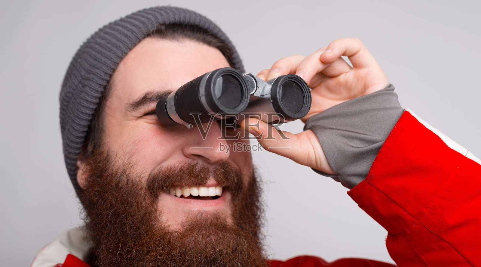 一位留着胡子的年轻攀登者微笑着透过双筒望远镜向外看。照片摄影图片