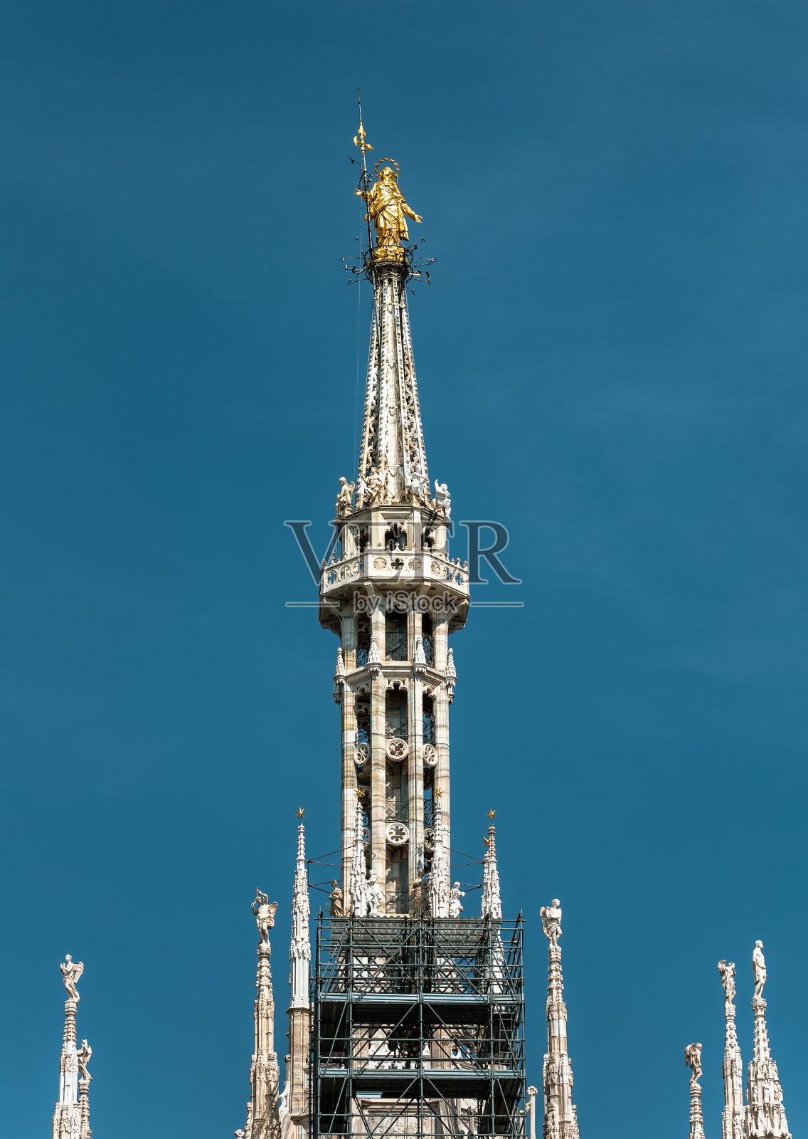 位于意大利米兰的圣母大教堂上，海拔108.5米。金色的圣母像在蓝天的背景塔尖上。照片摄影图片