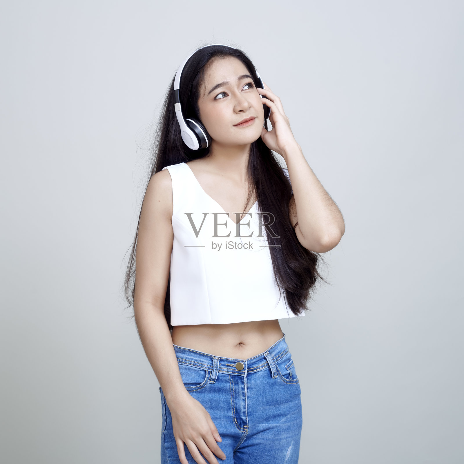 年轻的亚洲女人黑发长发微笑着听音乐与耳机隔离亮灰色背景照片摄影图片