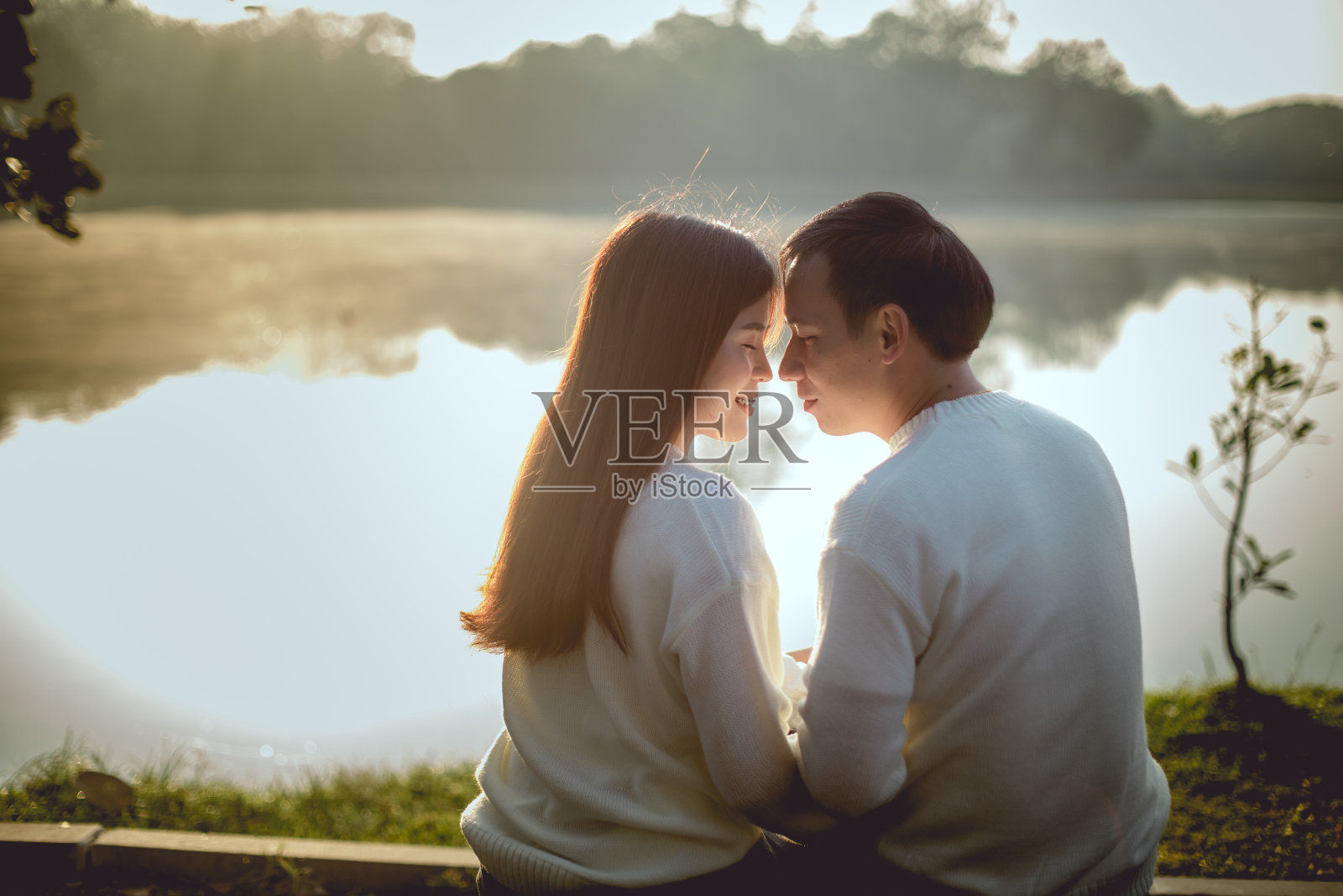 早上可爱的亚洲夫妇在湖公园的浪漫时光。他们将在一起接吻。照片摄影图片